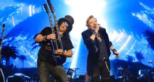 Slash, avec son célèbre chapeau haut-de-forme et sa guitare Les Paul, jouant sur scène avec Axl Rose, chantant avec énergie, lors d'un concert de Guns N' Roses.